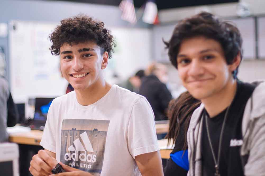 Two male engineering students at a table in a classroom smiling. Photo by Jeswin Thomas on Unsplash.